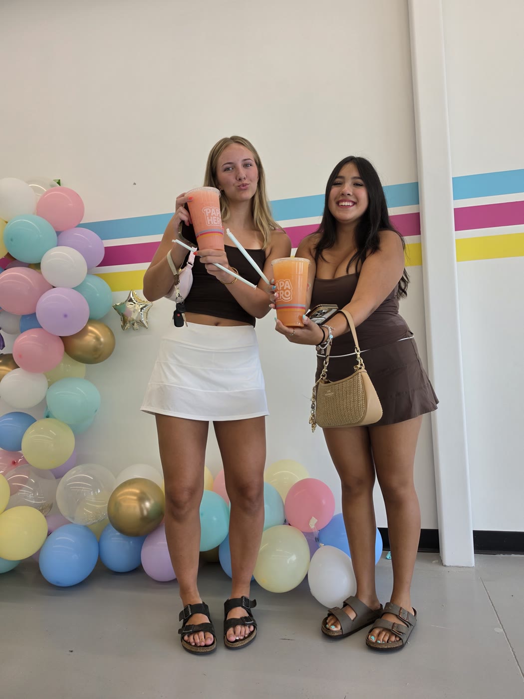Two guests holding orange Sparks in front of the cyan, pink, and yellow shop stripes.